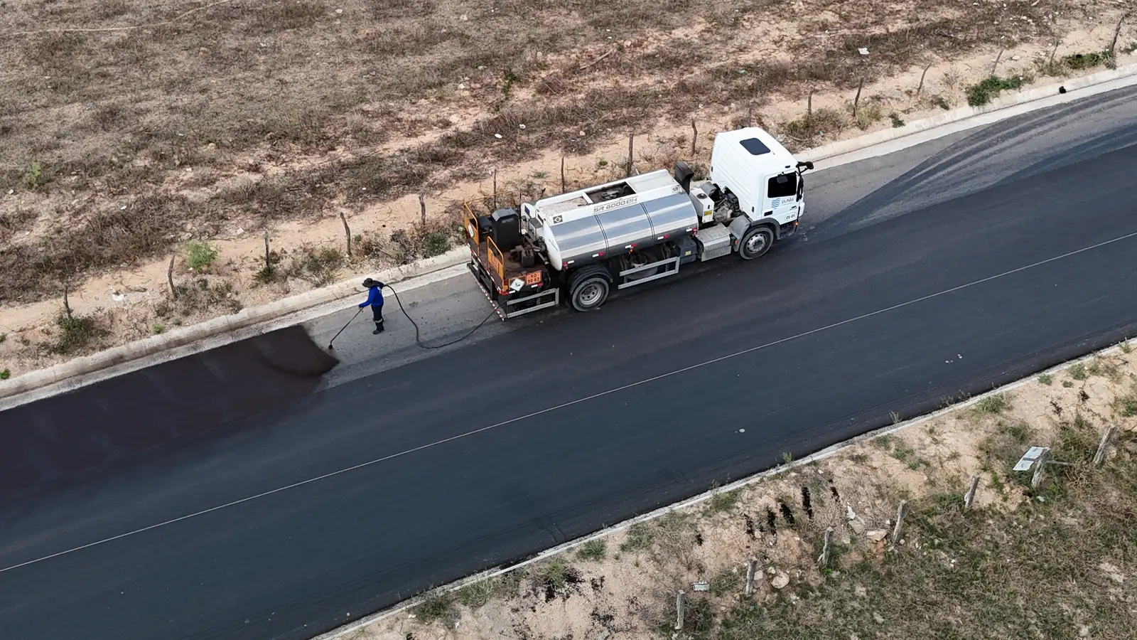Caminhão-tanque e trabalhador aplicando a imprimação no Acesso Pedrão