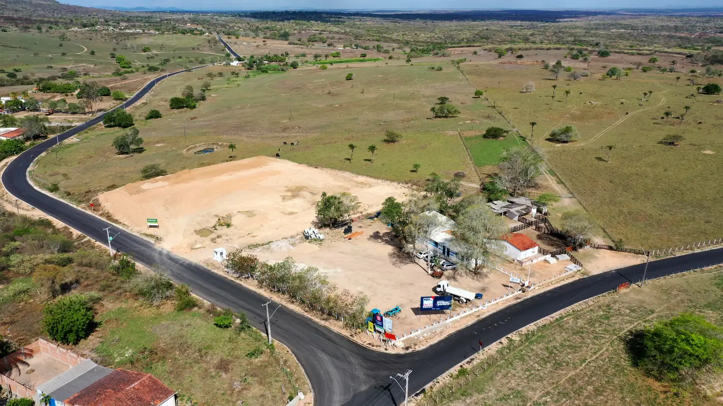 Vista aérea da pista asfaltada do Acesso Pedrão em curva, ao lado de um terreno em obras
