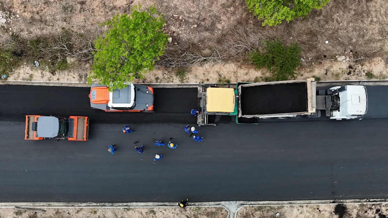 Vista de cima de caminhões e equipe na pavimentação do Acesso Pedrão