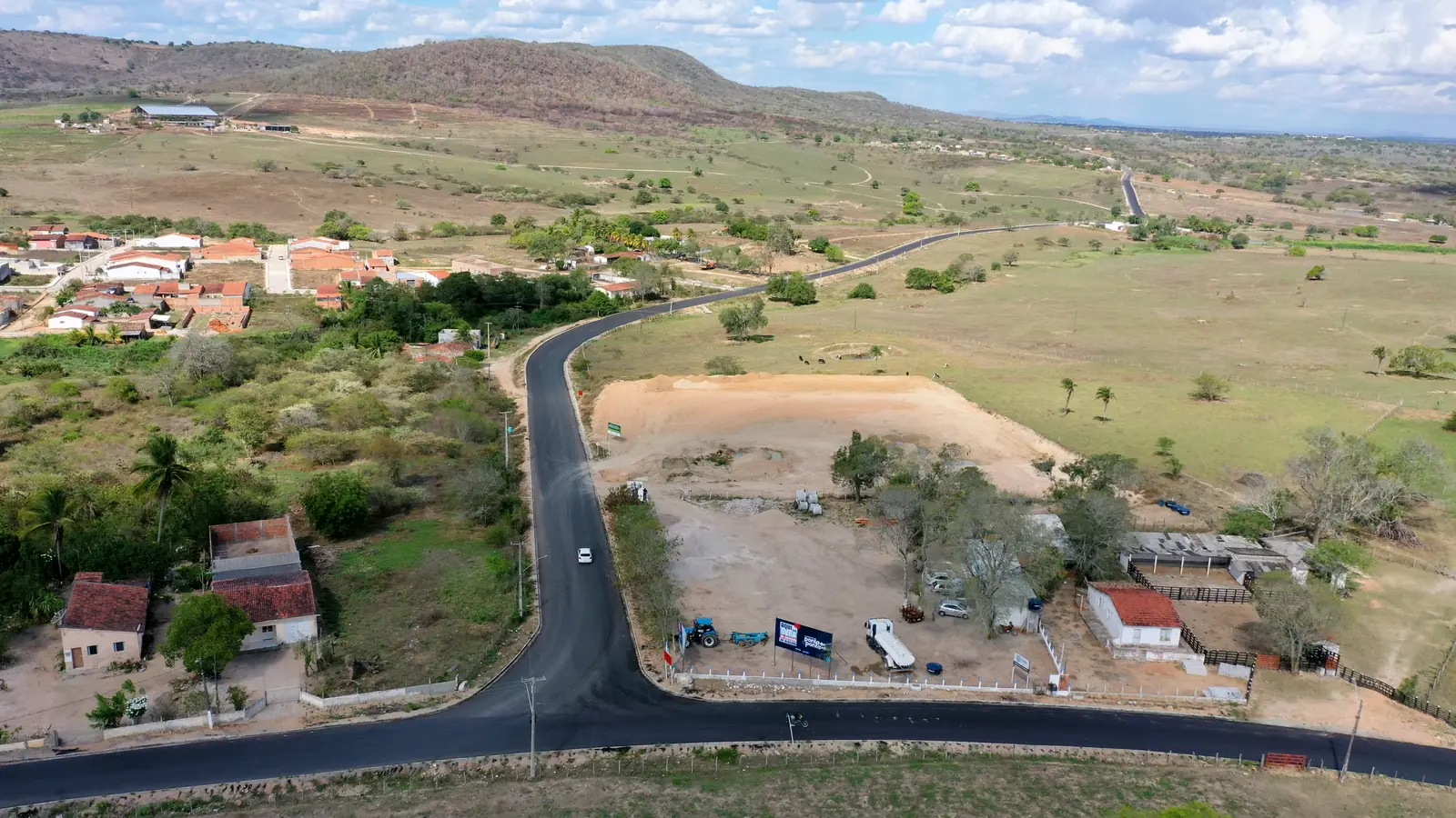 Vista aérea do Acesso Pedrão asfaltado, com casas ao fundo