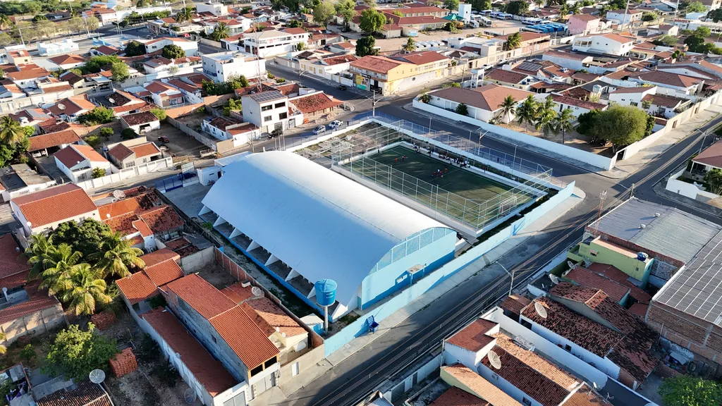 Vista aérea da quadra coberta e do campo ao lado, entre as casas
