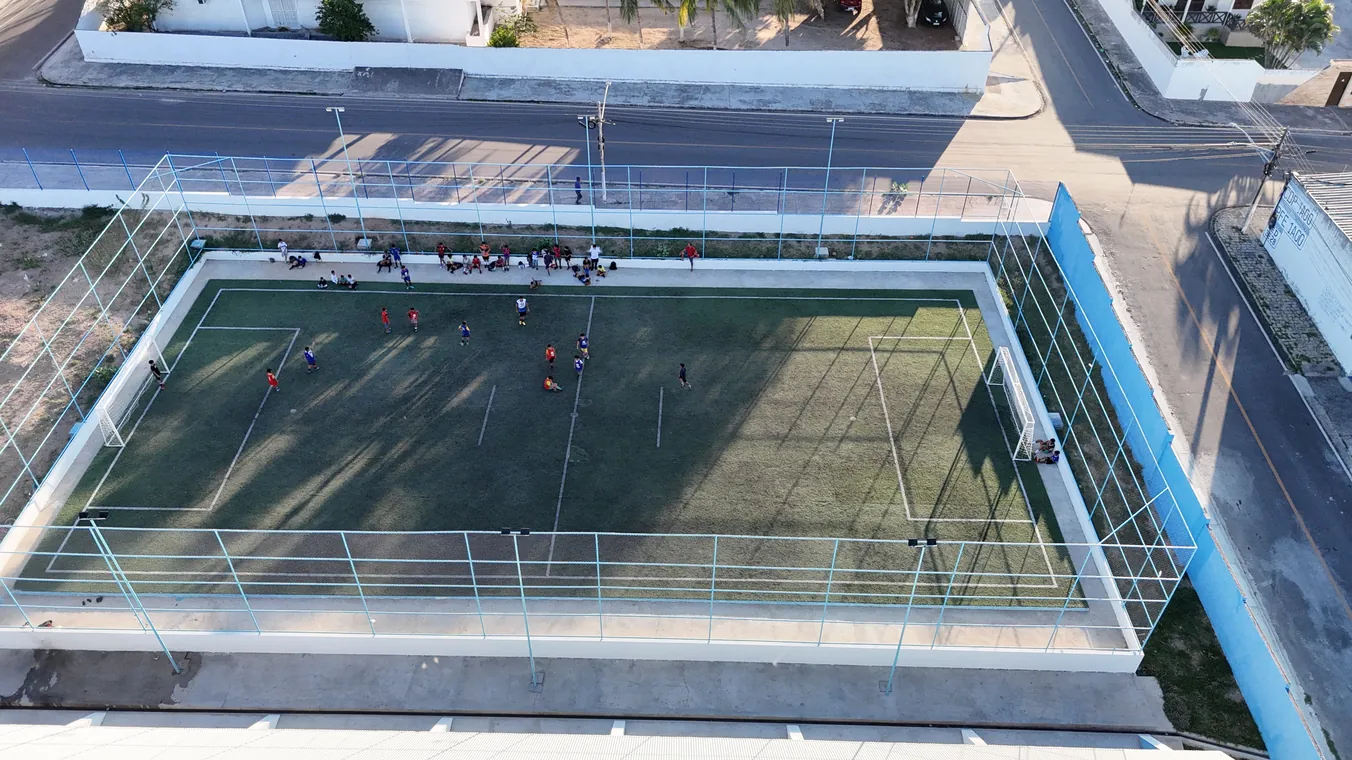 Campo de grama sintética com alambrado, ao lado da quadra, visto de cima